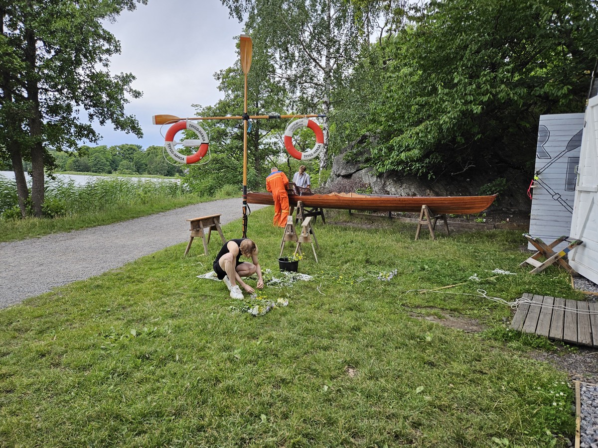 Club members restoring a wooden rowing boat outdoors, lifebuoys hung on an oar signpost