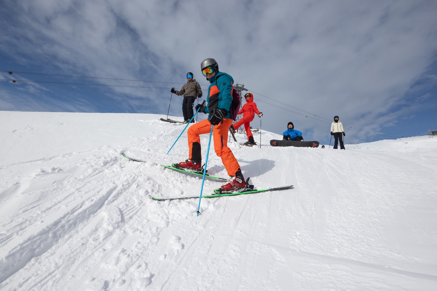 An alpine skier in orange pants setting off under a blue sky